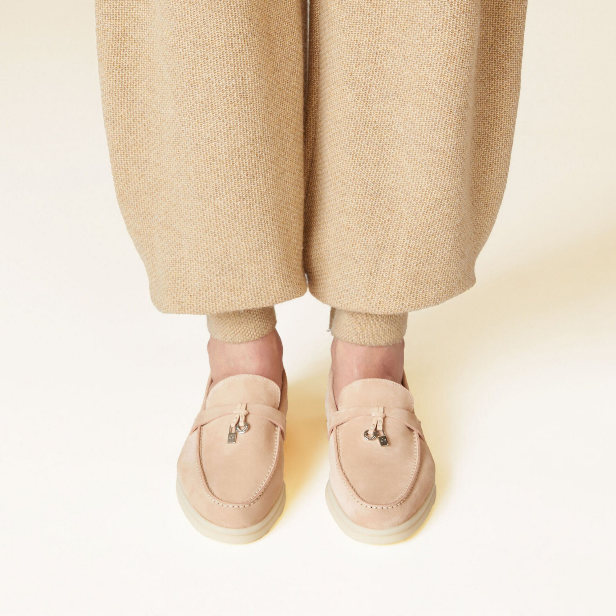 Person wearing beige loafers and pants on a light background