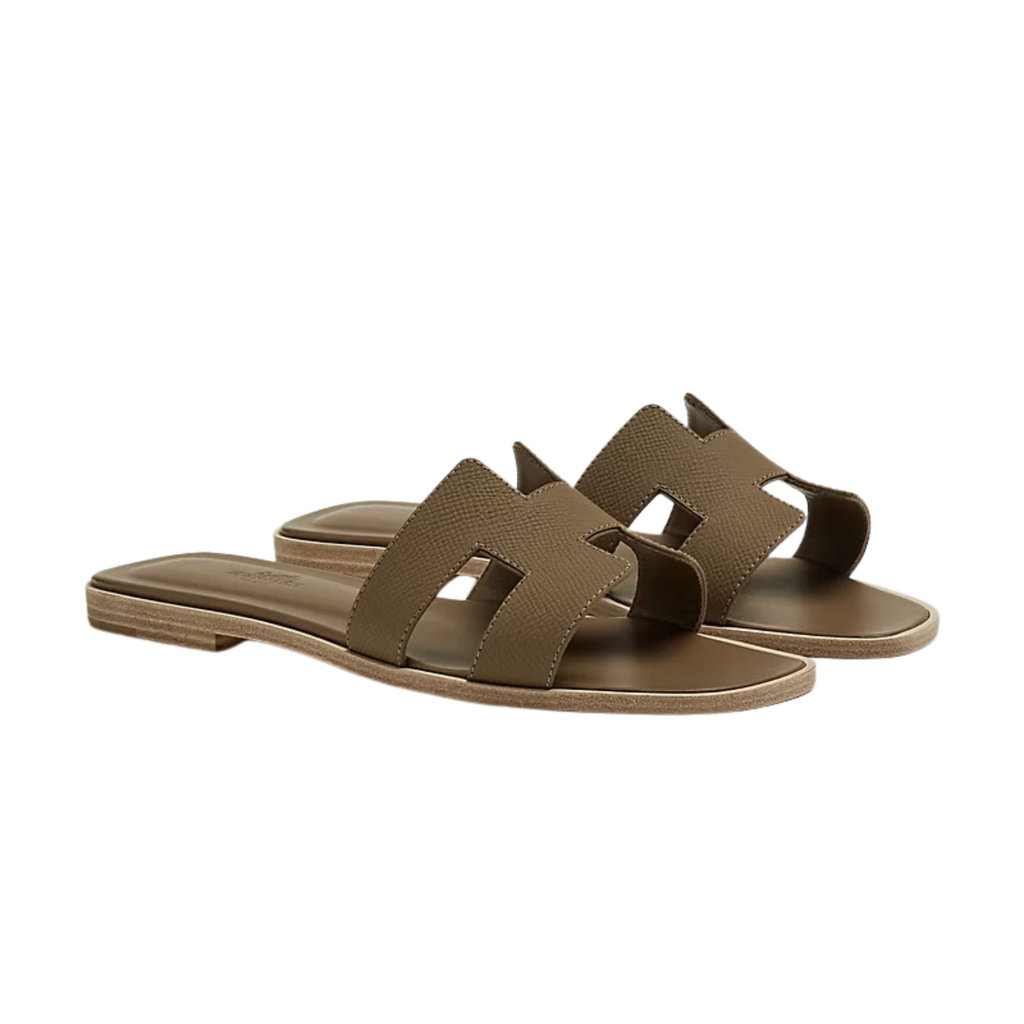Beige leather slide sandals with gold geometric detail on marble